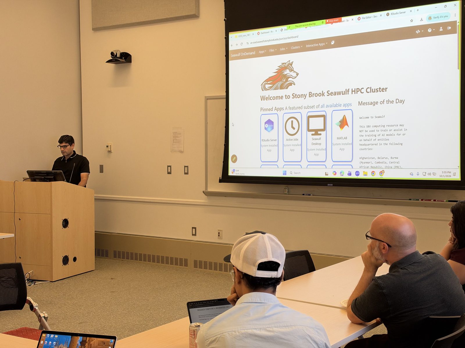 Arshad Mehmood at the podium beside the projected SeaWulf OnDemand dashboard and its pinned apps